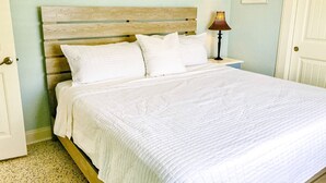A neatly made bed with a wooden headboard, white bedding, and a bedside lamp. - Nsb- Seaside Oasis (New Smyrna Beach)