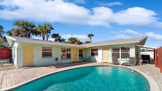 A house with a swimming pool, a patio with chairs, and palm trees in the background. - Nsb- Seaside Oasis (New Smyrna Beach)