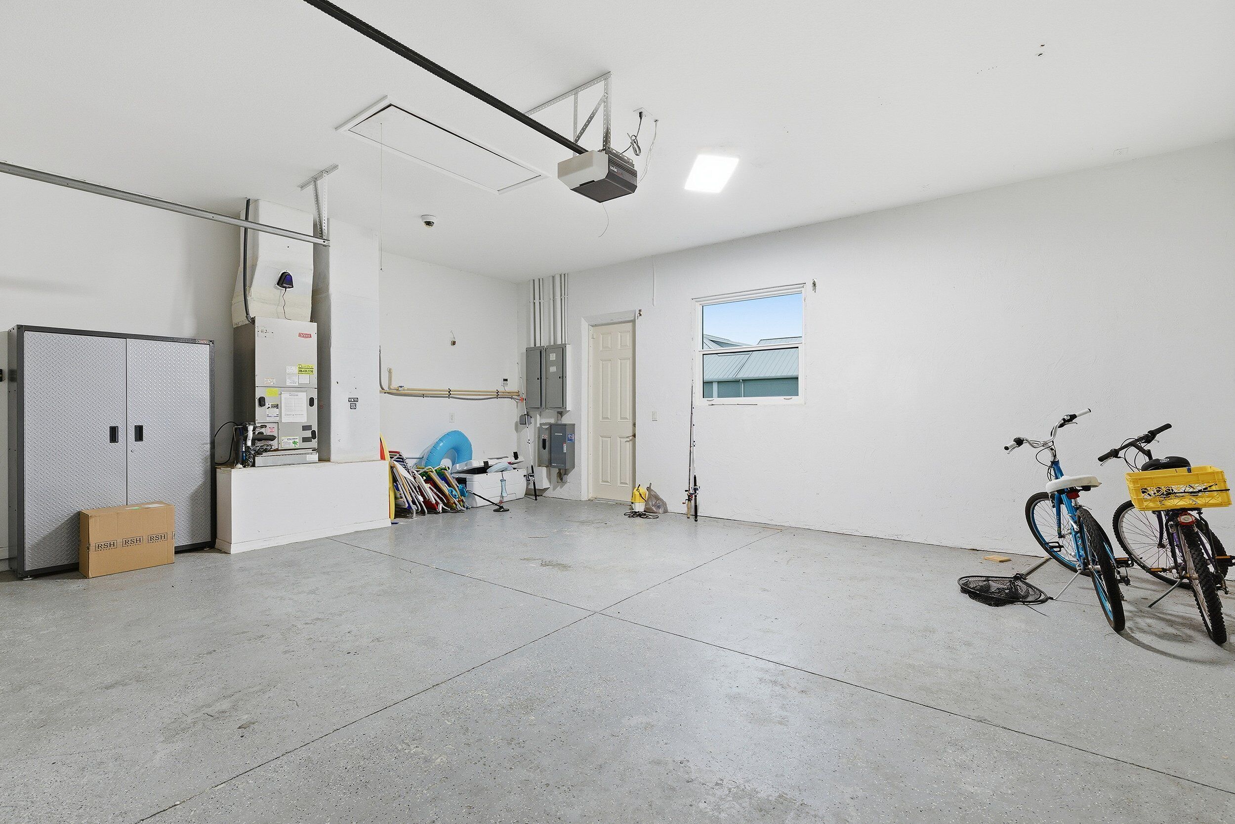 Un espace intérieur vaste et bien éclairé, avec une grande porte blanche, un projecteur fixé au plafond et des vélos appuyés contre le mur.