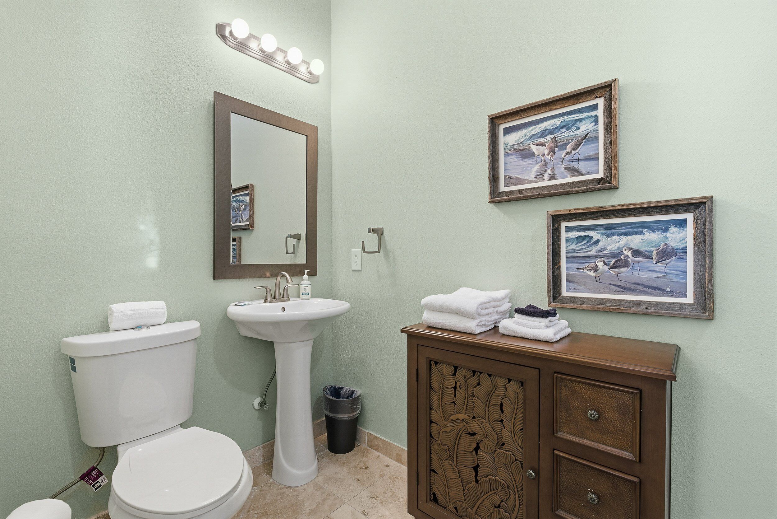 A bathroom with a toilet, sink, vanity, and framed pictures on the wall.