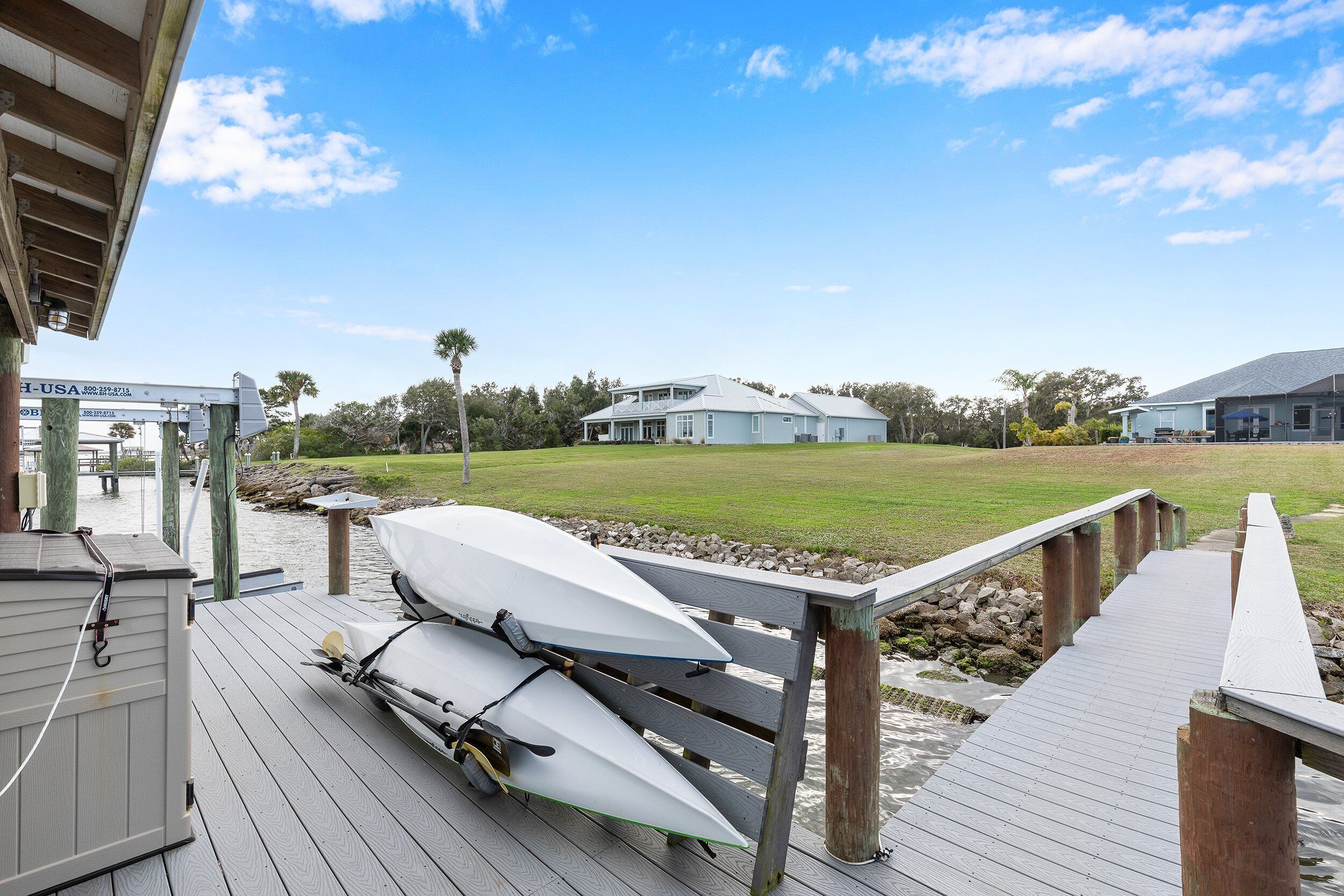 A wooden dock with boats, a grassy area, and a building in the background.