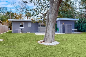 A residential property with a fenced yard, a tree, and a small building with a window and a door. - Daytona Pearl Cottage (Holly Hill)