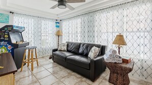 Ein Wohnzimmer mit einer schwarzen Ledersofa, einem hölzernen Hocker, einem kleinen Tisch mit einer Lampe und einer Karaoke-Anlage.