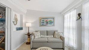 Ein Wohnzimmer mit grauem Sofa, einem runden Couchtisch und einem Gemälde einer Strandansicht.
