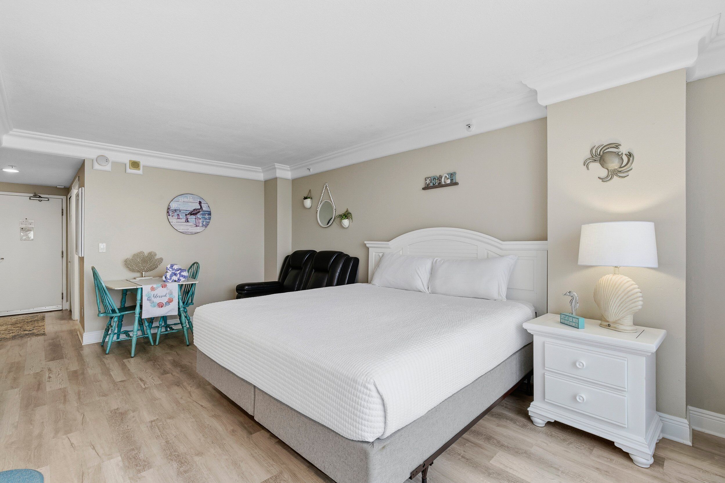 Een slaapkamer met een groot bed, een nachtkastje met een lamp, een stoel en een tafeltje met een decoratief object.