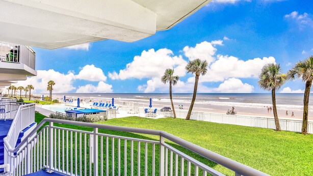 A balcony with a view of the beach, palm trees, and a pool area. - Daytona Surfside Club 109- Blue Umbrella (Daytona Beach Shores)