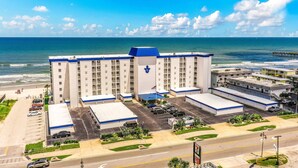 A multi-story hotel with a parking lot and a view of the ocean. - Daytona Surfside Club 109- Blue Umbrella (Daytona Beach Shores)