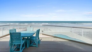 A wooden deck with a table and chairs, overlooking a beach and ocean. - Daytona Atlantic Sunrise Home (Daytona Beach Shores)