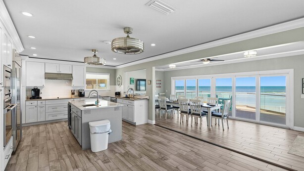 A modern kitchen with a central island, a dining area with a view, and a large window overlooking the ocean. - Daytona Atlantic Sunrise Home (Daytona Beach Shores)