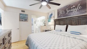 Ein Schlafzimmer mit einem Bett, einem Deckenventilator, einer Wand mit dem Schriftzug 'Let's Snuggle', einem Gemälde und einer Kommode.