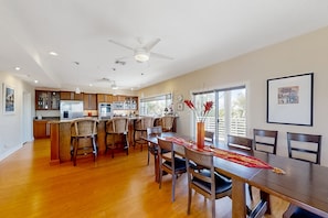 A spacious kitchen with modern appliances, a dining area with wooden furniture, and large windows offering natural light. - NSB Indian River Waterfront Gem (New Smyrna Beach)