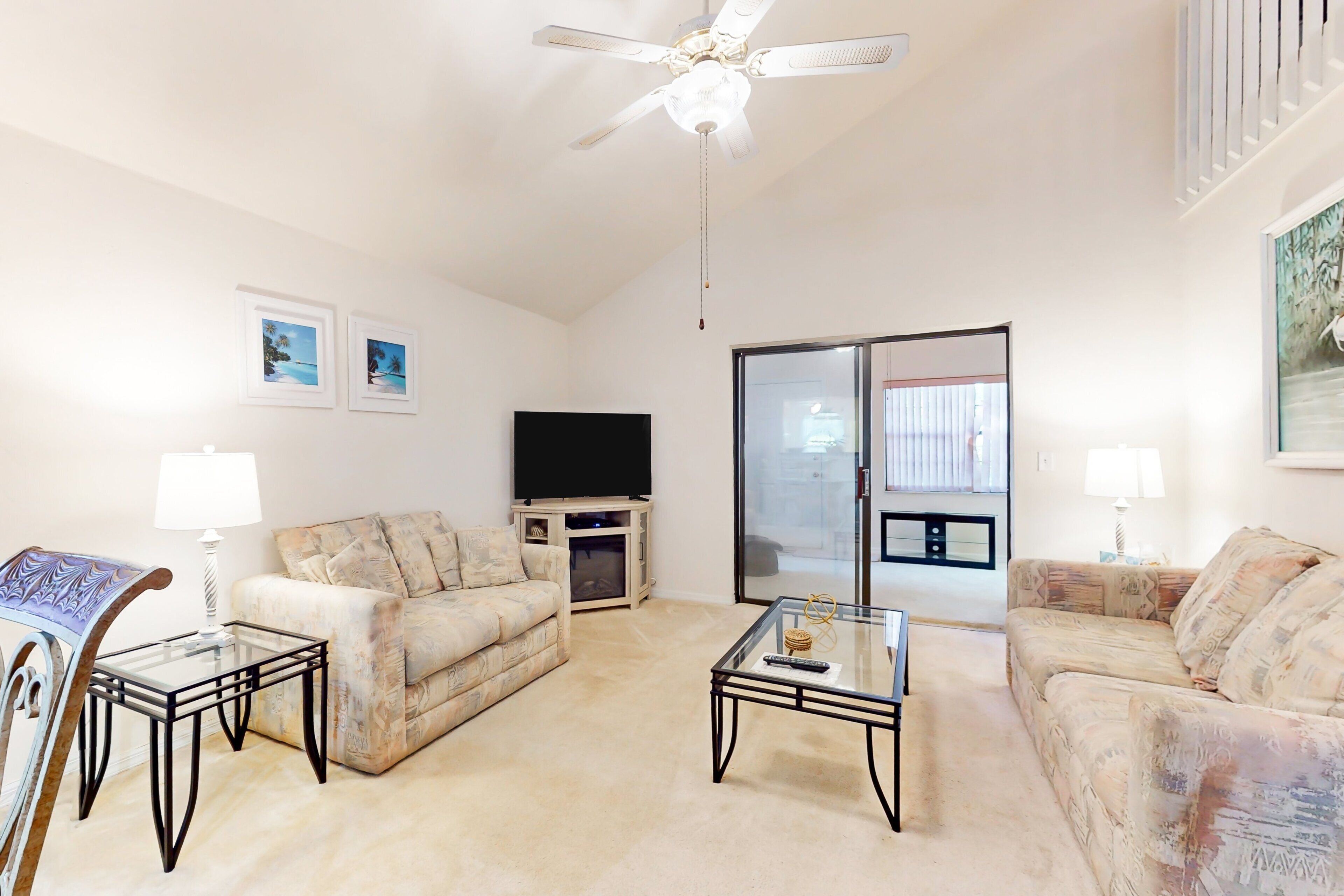 A living room with two sofas, a glass coffee table, a TV, and a ceiling fan.