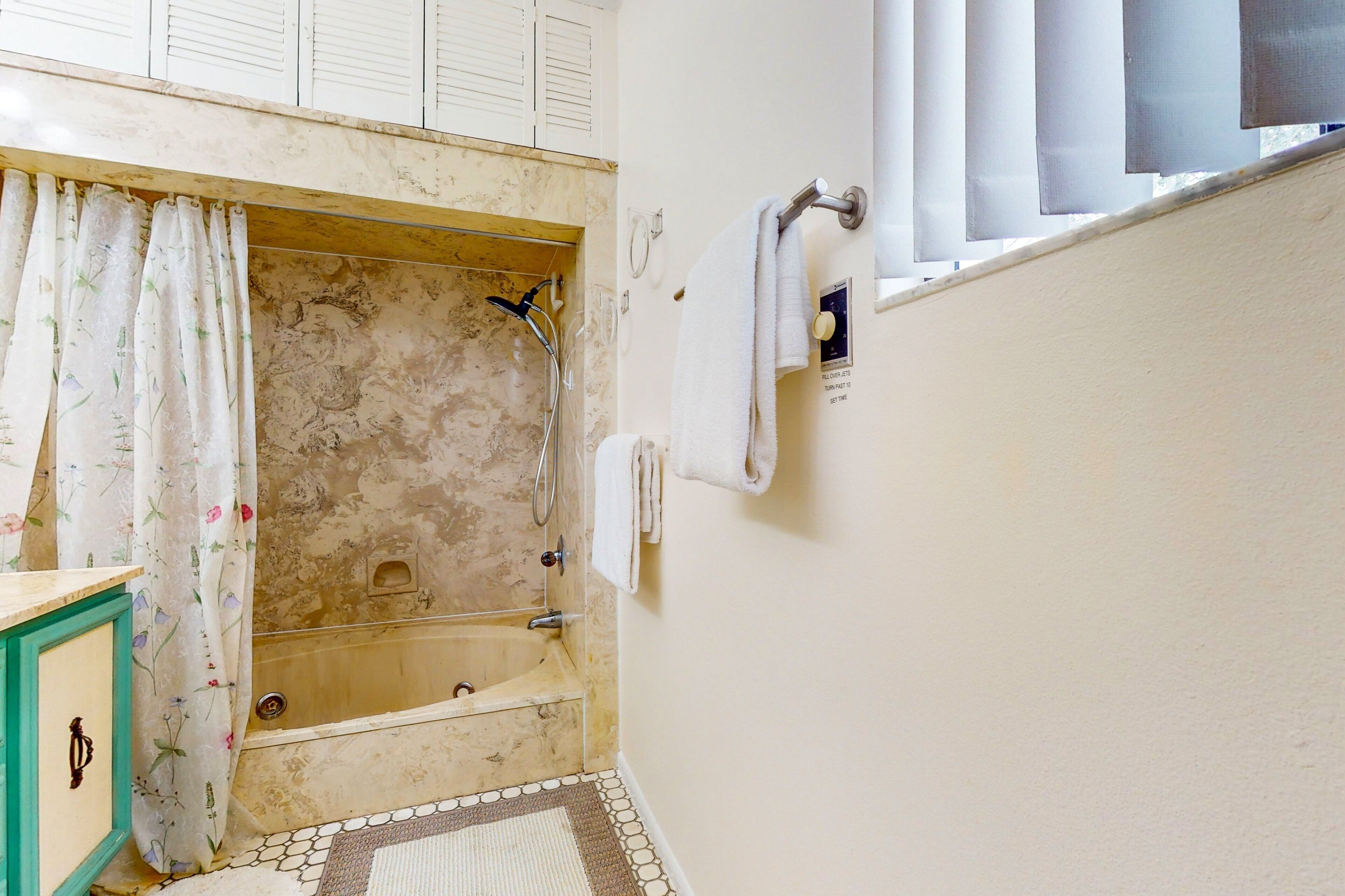 A bathroom with a bathtub, a shower, a towel rack, and a window with blinds.