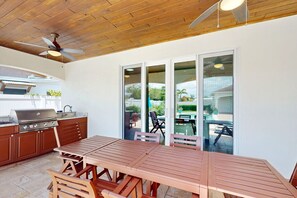 An outdoor kitchen area with a grill, wooden table, and chairs. - NSB Pearl By The Sea (New Smyrna Beach)