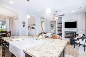 A modern kitchen with a large island, a dining area with chairs, a fireplace, and a TV mounted on the wall. - NSB Pearl By The Sea (New Smyrna Beach)