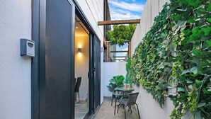 Una moderna veranda esterna con una porta scorrevole in vetro che dà su un'stanza, un tavolino rotondo con sedie e un muro ricoperto d'edera.