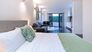 Una camera d'albergo moderna con un letto grande, un divano, un'area pranzo e vista sull'esterno.
