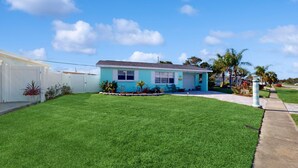A single-story house with a blue exterior, a well-maintained lawn, and a clear sky. - Seaside Escape (Ormond Beach)