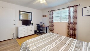 A bedroom with a bed, a desk, a chair, a ceiling fan, a television, and curtains. - Seaside Escape (Ormond Beach)