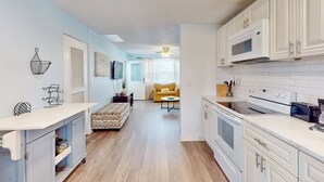 A compact kitchen with white cabinets, a microwave, and a stove. There is a yellow sofa in the background and a small table with a plant. - Seaside Escape (Ormond Beach)