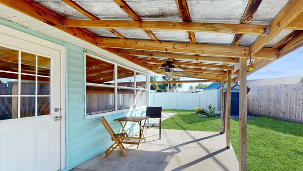 A covered patio area with a wooden ceiling, a table, and chairs. - Seaside Escape (Ormond Beach)