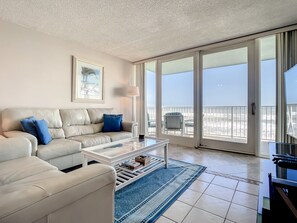 A living room with a beige sofa, a coffee table, and a view of the beach through large sliding glass doors. - Smyrna Beach Club 307 (New Smyrna Beach)