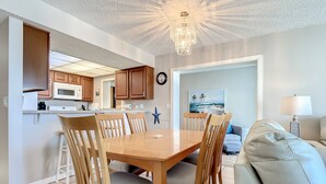 A modern kitchen with wooden cabinets, a microwave, and a dining area with a wooden table and chairs. - Smyrna Beach Club 307 (New Smyrna Beach)
