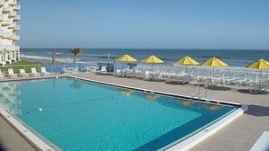 A swimming pool with a clear view of the ocean, a building with balconies, and yellow umbrellas. - Smyrna Beach Club 307 (New Smyrna Beach)