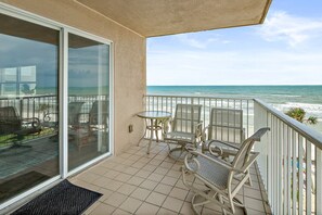 Un balcone con vista sull'oceano, arredato con sedie e un tavolo.