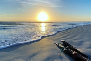 Una spiaggia con un tronco sulla sabbia e il sole che si riflette sull'acqua.
