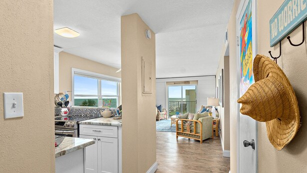 A kitchen with white cabinets, a countertop, and a window. There is a wicker wall hanging and a door with a handle. - NSB Sea Coast 401 (New Smyrna Beach)