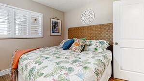 A bedroom with a bed, a window with blinds, a wall-mounted decorative plate, and a door. - NSB Sea Coast 401 (New Smyrna Beach)