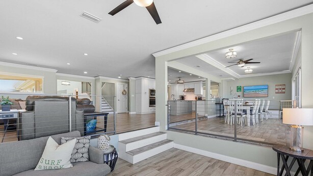 A spacious living area with a grey sofa, a staircase leading to a balcony, and a kitchen in the background. - Atlantic Sunrise Home Plus Cottage (Daytona Beach Shores)