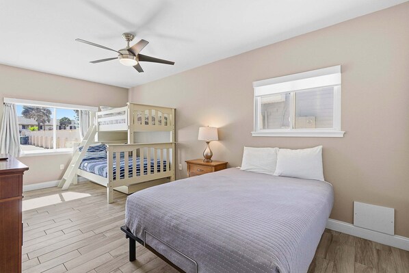 A bedroom with a bed, a nightstand, a lamp, a ceiling fan, a window, and a view of the outside. - Atlantic Sunrise Home Plus Cottage (Daytona Beach Shores)