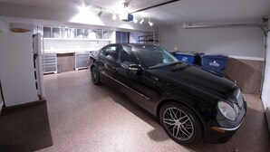 A black car parked in a well-lit garage with a kitchen area in the background. - Quiet 3BR Home Near Hospital, Finished Basement, Fast WiFi (Elgin)