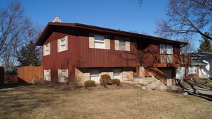 A two-story house with a wooden deck and a front porch. - Quiet 3BR Home Near Hospital, Finished Basement, Fast WiFi (Elgin)