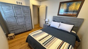A bedroom with a bed, a nightstand, a dresser, and a door leading to another room. - Quiet 3BR Home Near Hospital, Finished Basement, Fast WiFi (Elgin)