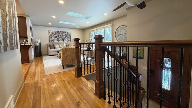 A spacious living area with a wooden staircase, a ceiling fan, and a large clock on the wall. - Quiet 3BR Home Near Hospital, Finished Basement, Fast WiFi (Elgin)