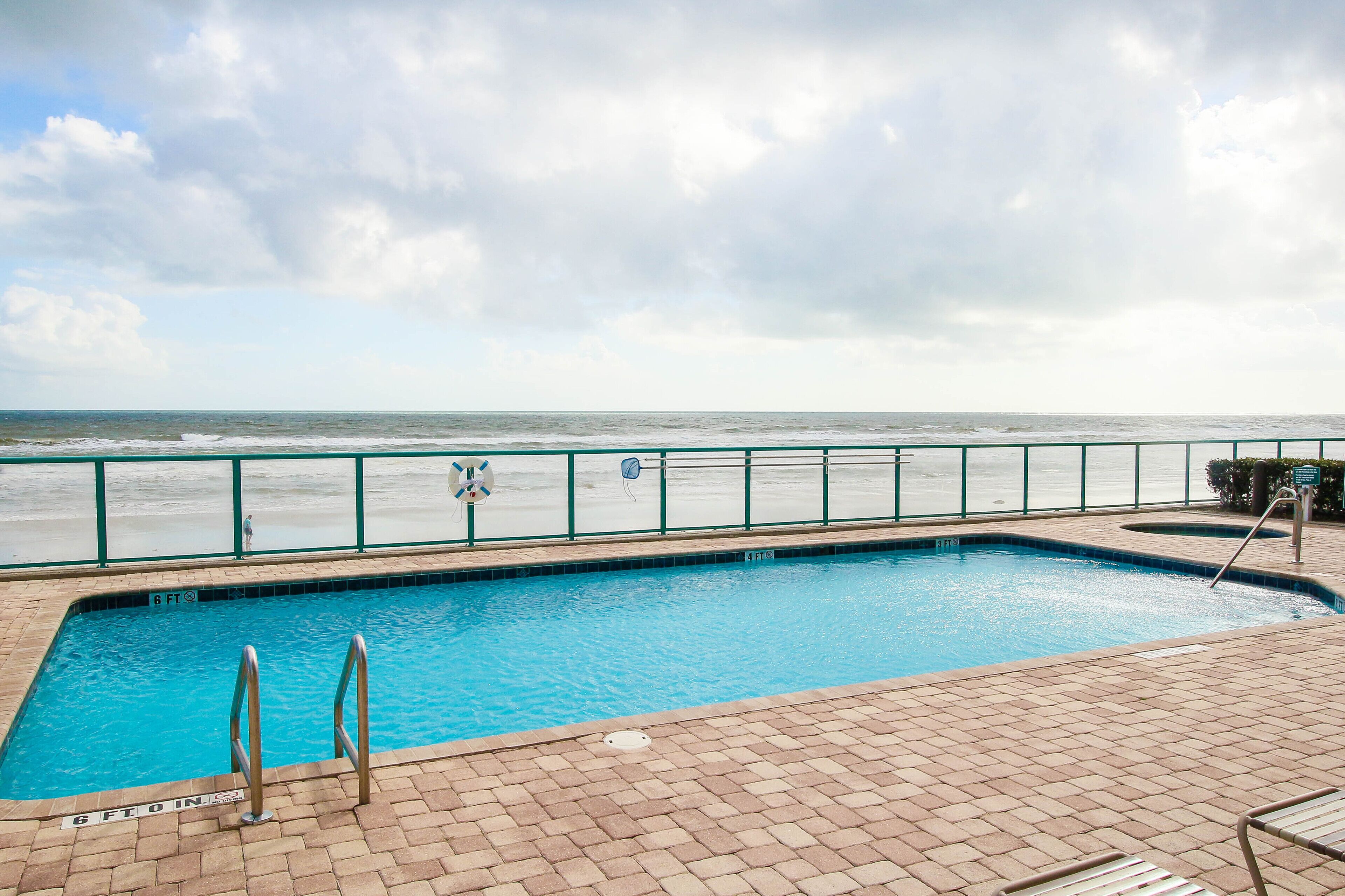 A swimming pool with a view of the ocean, a lifeguard stand, and a brick deck.