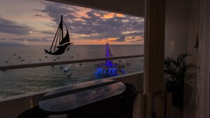 Vista desde un balcón sobre una masa de agua con barcos, una estructura distante con luces azules y un adorno con forma de vela.