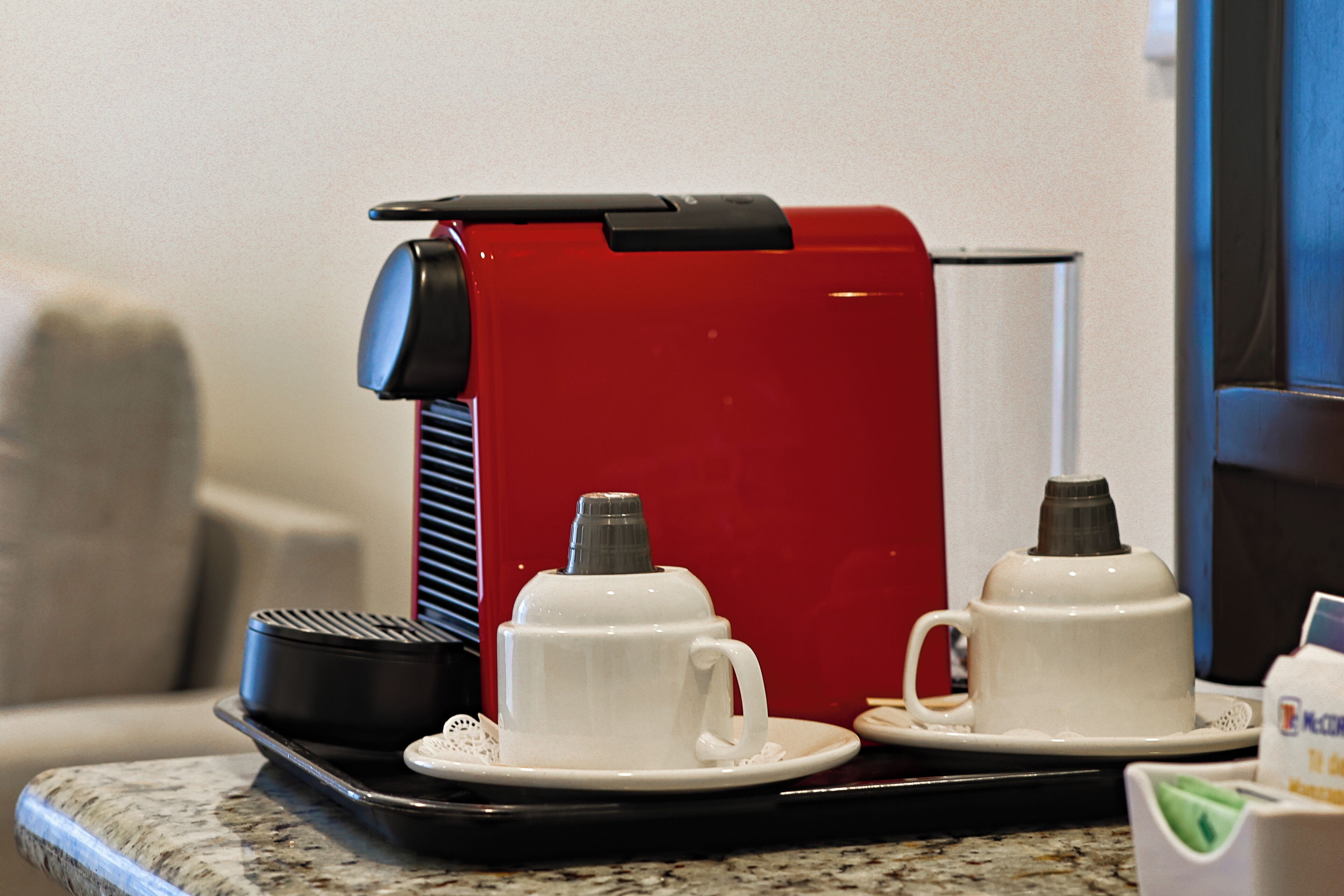 Eine Kaffeemaschine mit zwei weißen Tassen auf einer Ablage, eine schwarze Kaffeekanne und eine weiße Kaffeekanne auf einer Arbeitsplatte.