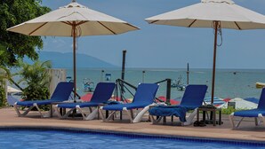 Zona junto a la piscina con sillones de descanso y sombrillas, con vista a un cuerpo de agua.