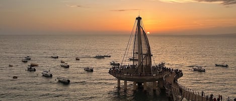 Eine Küstenansicht mit einer Brückenstruktur über dem Wasser, Strandbesuchern und Booten.