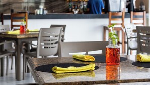 Un interior de restaurante con una zona de bar, asientos y una mesa con un florero de vidrio y servilletas.