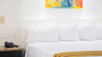 Ein Hotelzimmer mit einem Bett, weißen Kissen, einem Telefon und einem farbenfrohen, abstrakten Gemälde an der Wand.