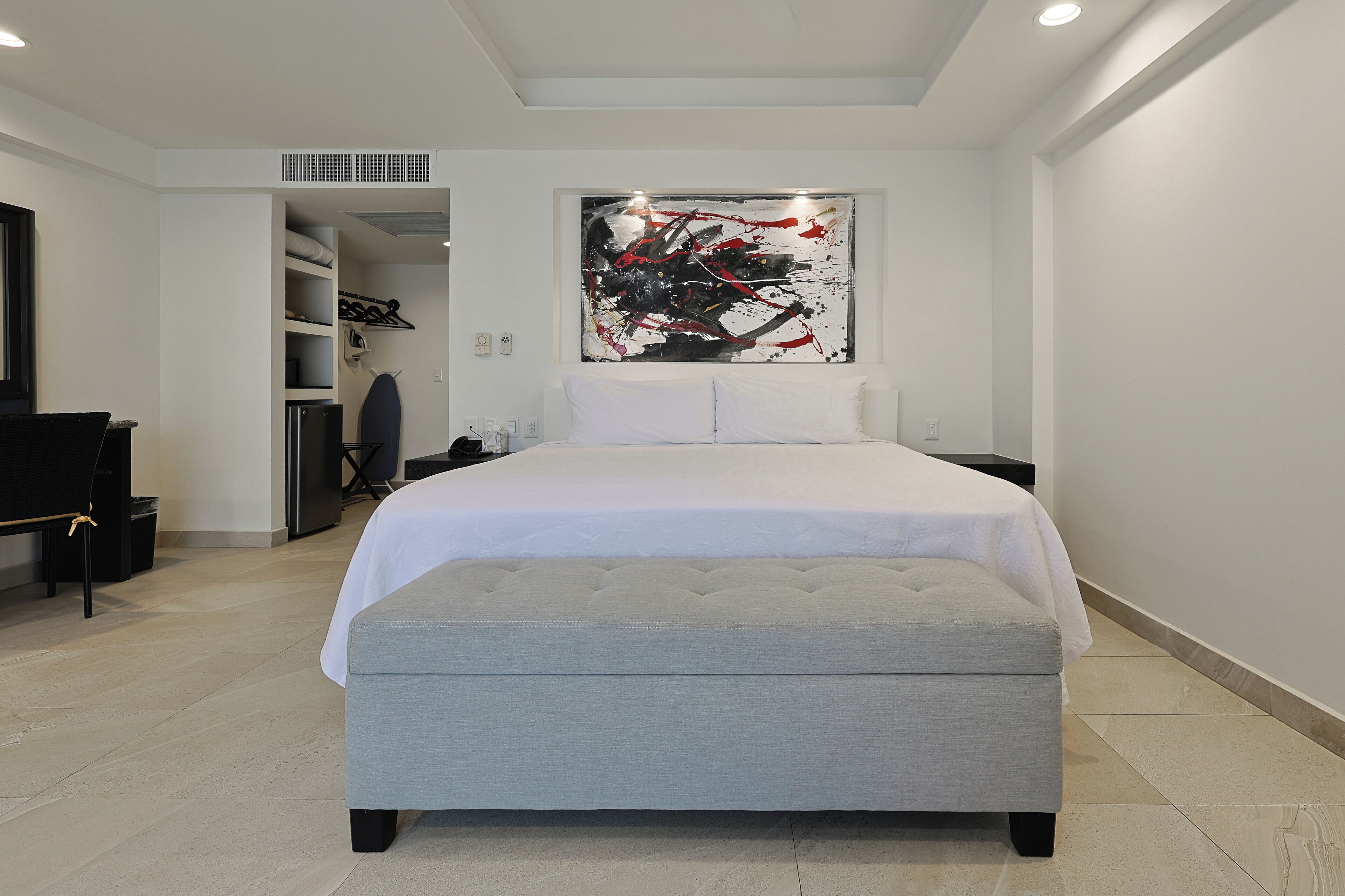 A modern bedroom with a large bed, a wardrobe, and a painting on the wall.