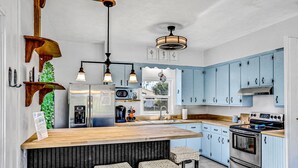 Eine moderne Küche mit blauen Schränken, einer Holzinsel, Edelstahlgeräten und Pendelleuchten.