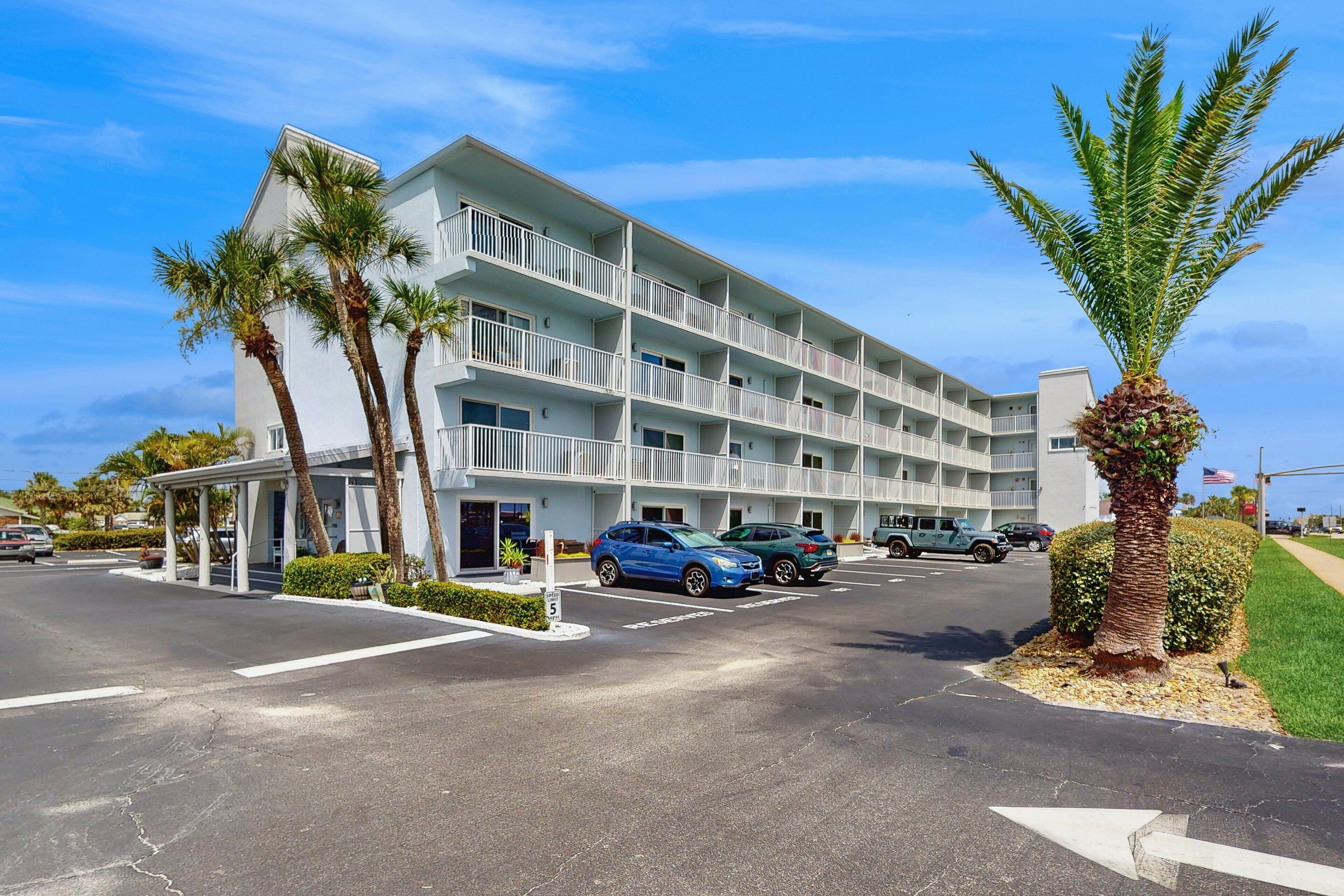 A multi-story hotel with balconies, parking spaces, and palm trees.