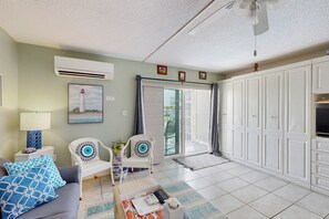 A living room with a sofa, two patterned chairs, a coffee table, and a TV. There is a sliding glass door leading to a balcony. - Mariners Cove 302 (New Smyrna Beach)