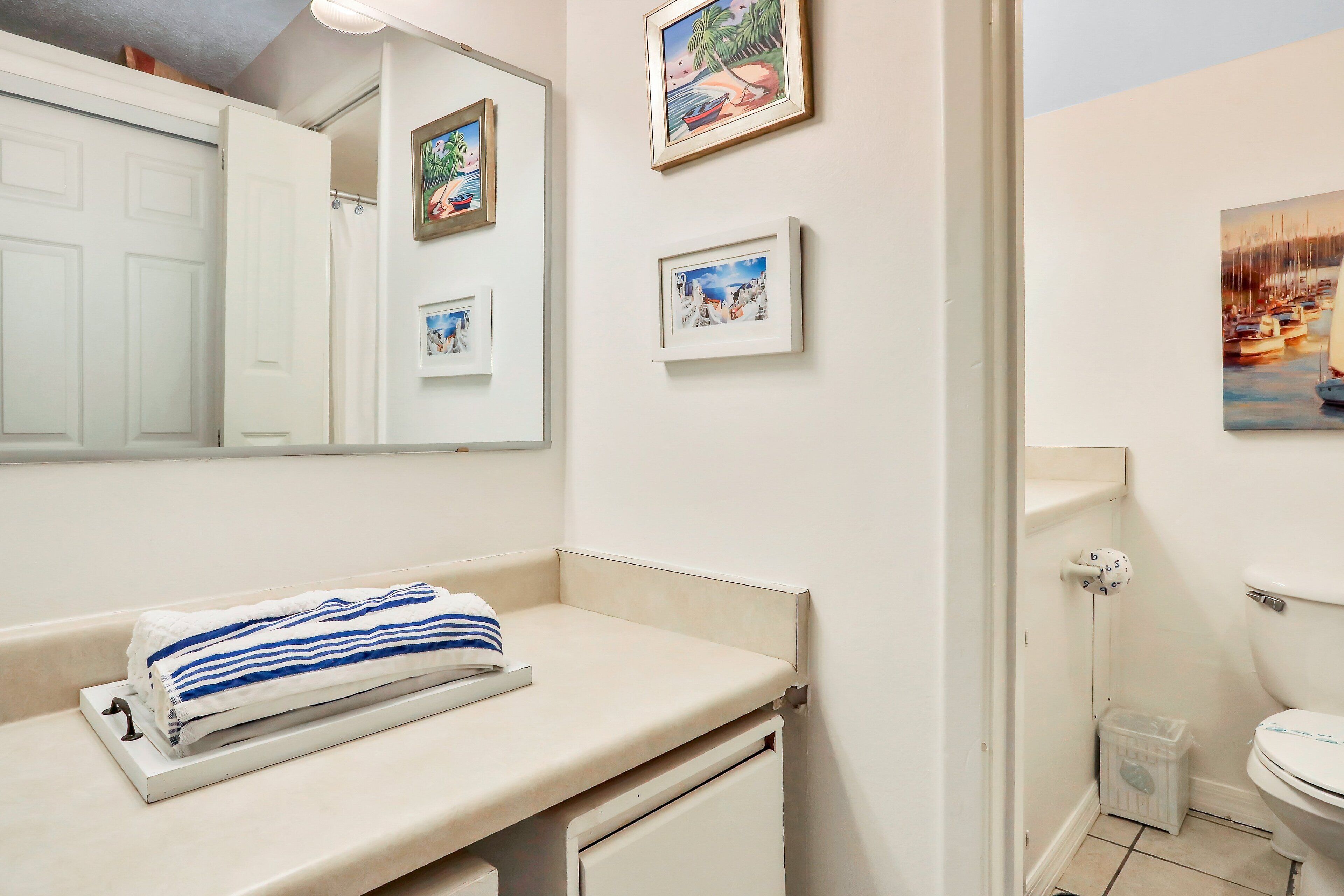 A bathroom with a white sink, a towel, a mirror, and framed pictures on the wall.